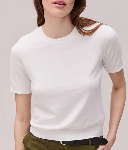 Woman wearing a white t-shirt and green pants against a plain background