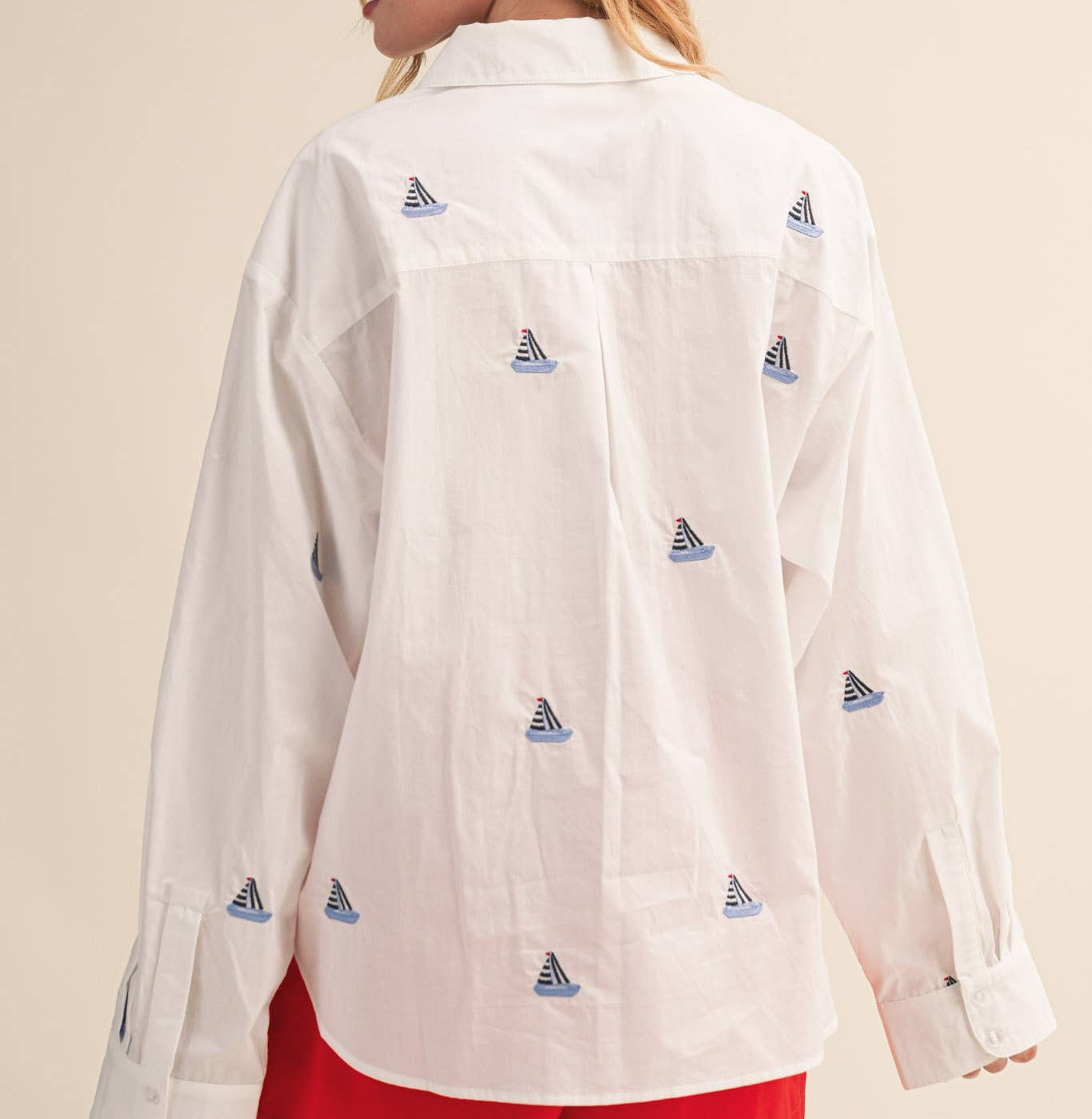 Woman wearing a white shirt with sailboat patterns and red shorts on a beige background