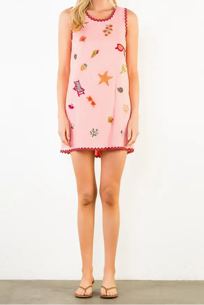 Woman wearing a pink dress with colorful embroidery on a white background