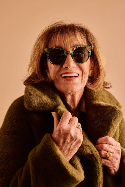 Woman wearing sunglasses and a green coat against a beige background