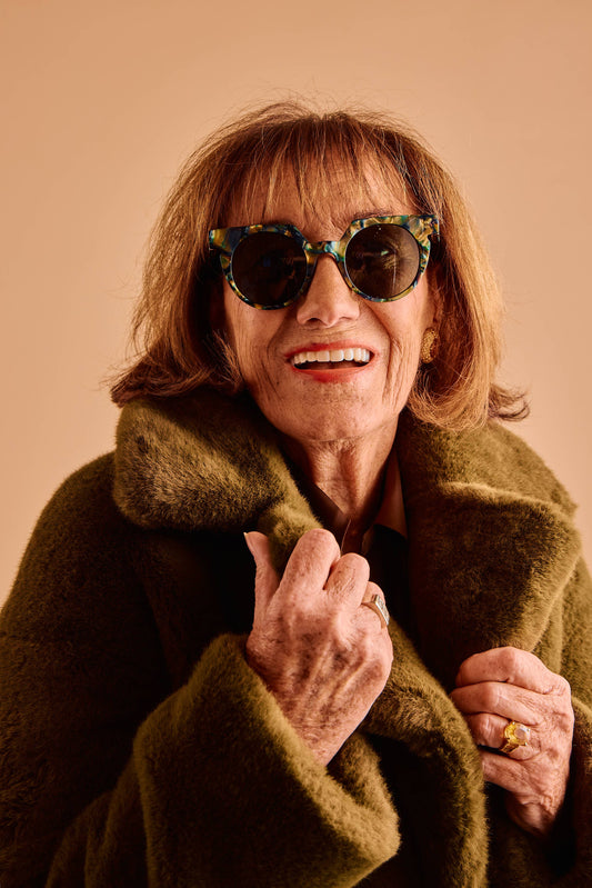 Woman wearing sunglasses and a green coat against a beige background