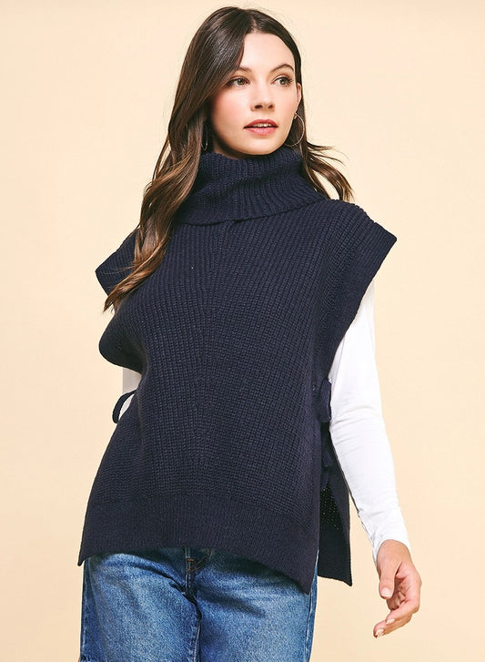 Woman wearing a navy blue knitted vest over a white shirt on a beige background