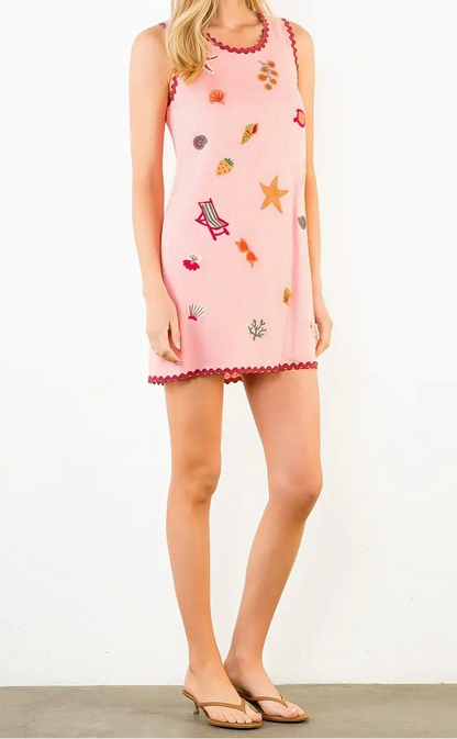 Woman wearing a pink dress with colorful patterns on a white background