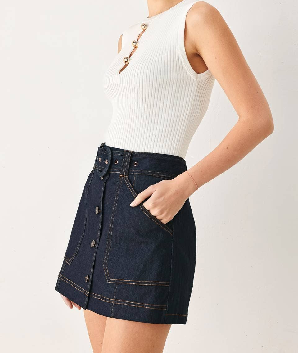 Woman wearing a white sleeveless top and dark denim skirt on a plain background