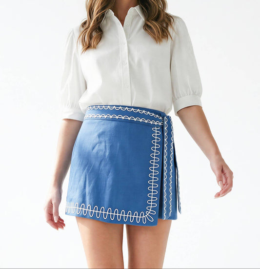 Woman wearing a white blouse and blue skirt with white embroidery on a white background