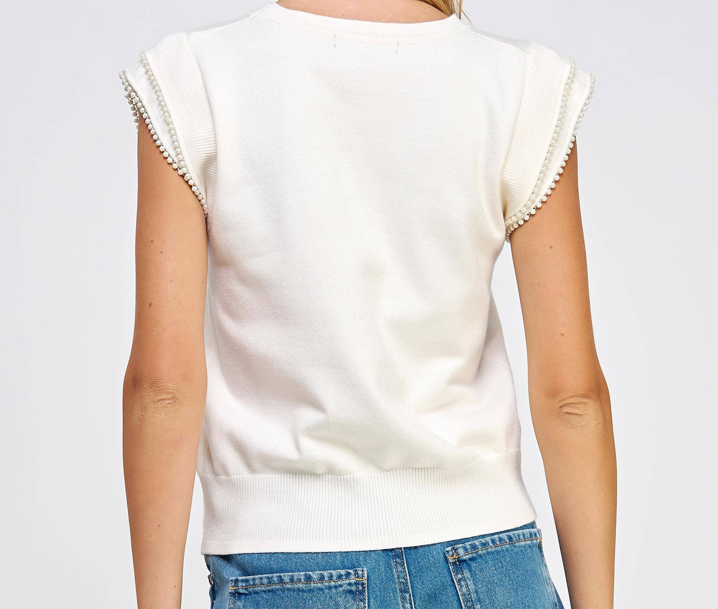 Woman wearing a white sleeveless top and blue jeans on a light gray background