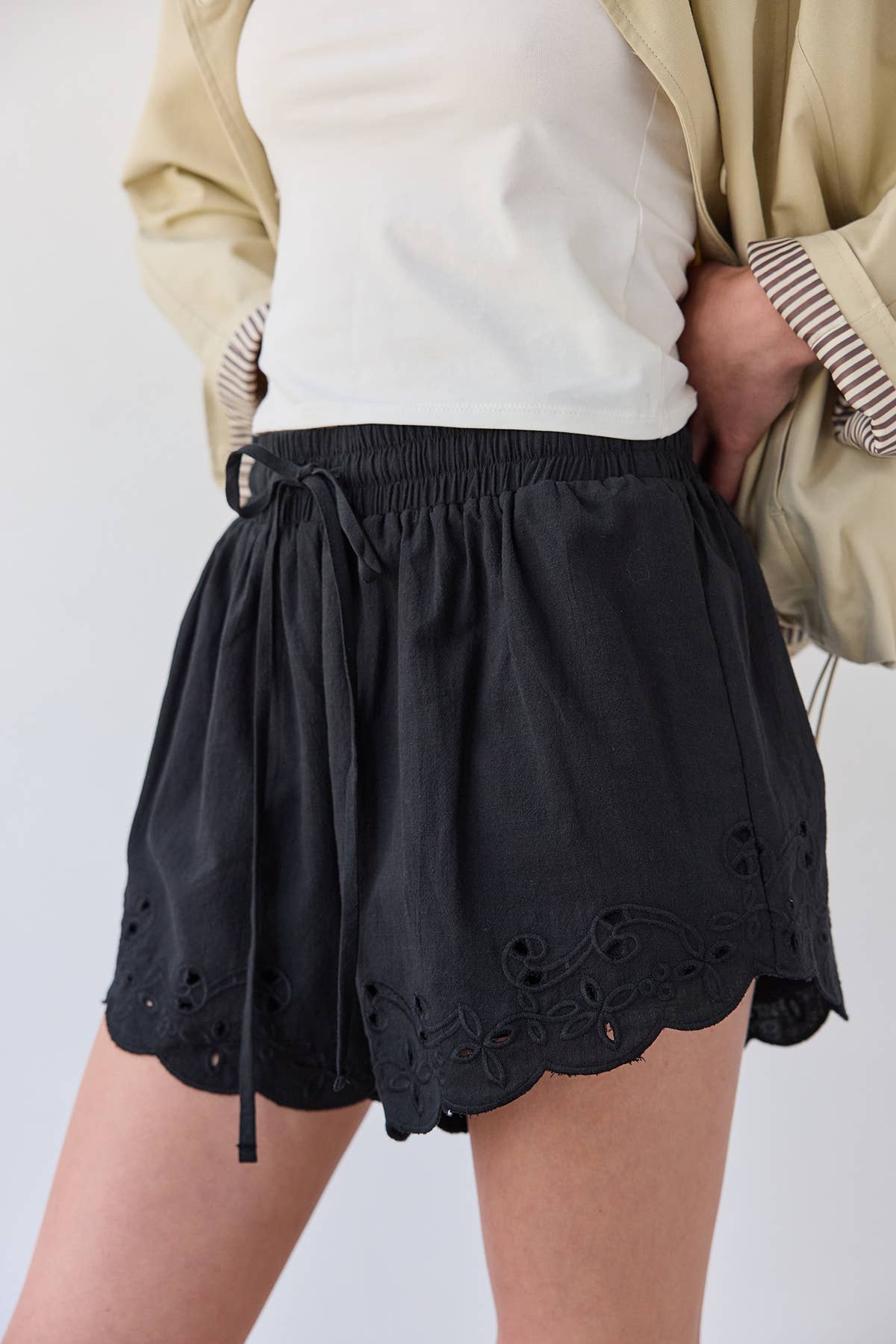 Black shorts with eyelet details worn by a person on a plain background