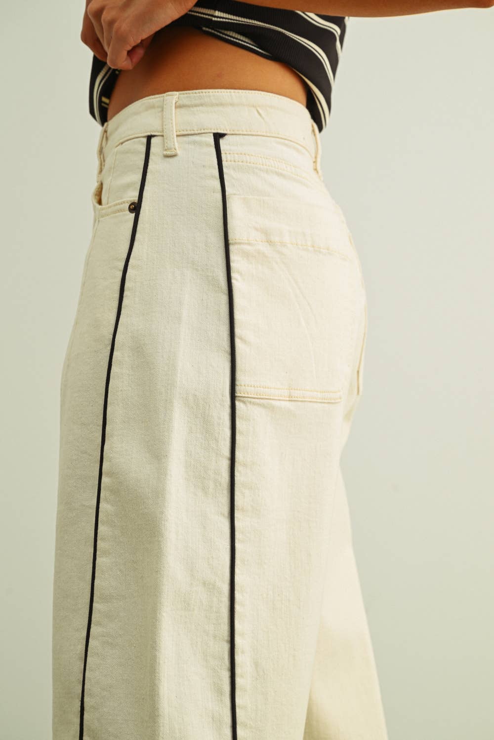Beige pants with black piping on a plain background