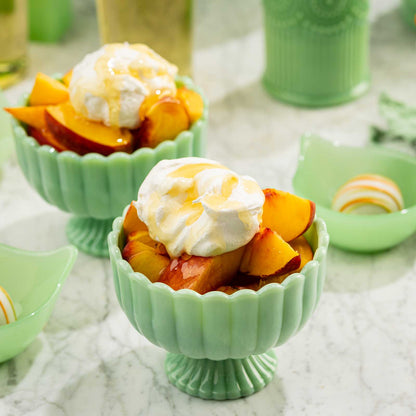 Green bowls filled with peach slices and whipped cream on a textured surface.