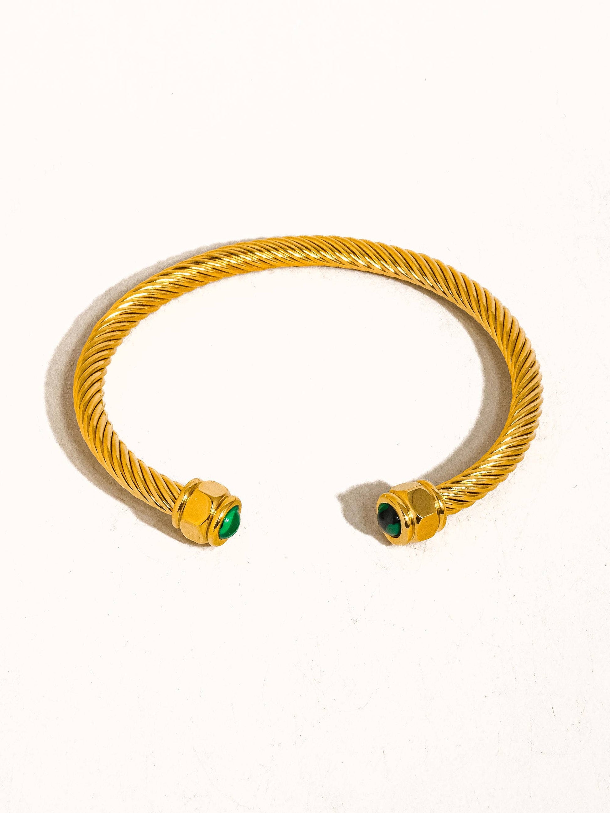 Gold bracelet with green gemstones on a white background