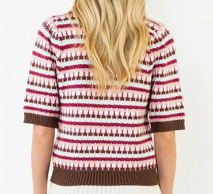 A woman viewed from the back wearing a short-sleeve knit top with horizontal geometric stripes in brown, pink, and white, paired with a white pleated skirt, against a plain white background.