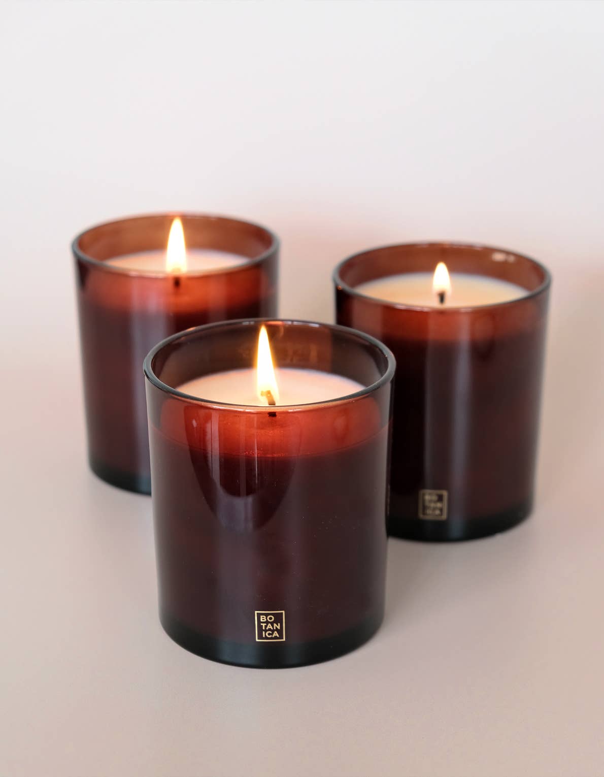 Three lit candles in brown glass containers on a light background