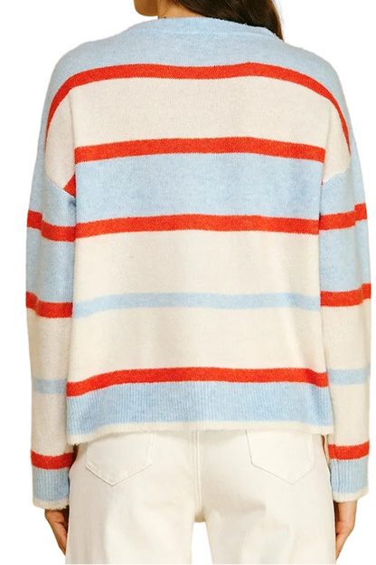 A woman shown from the back wearing a knit sweater with horizontal stripes in light blue, red, and off-white, paired with white pants against a solid beige background.
