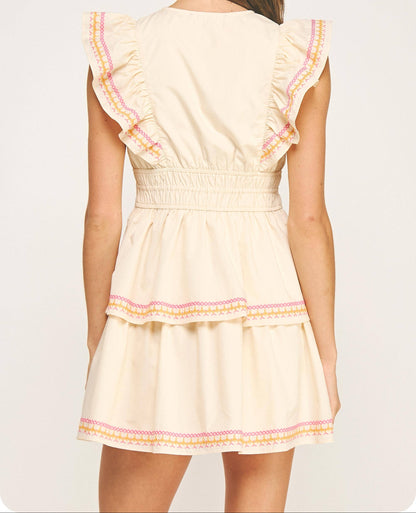 Woman wearing a cream-colored dress with ruffled sleeves and hem on a white background