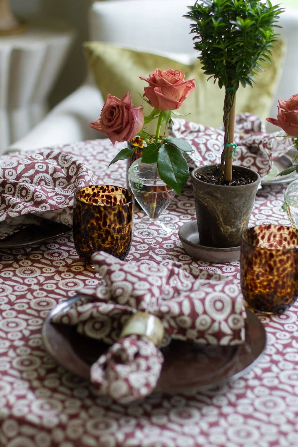 Decorative table setting with patterned tablecloth, candles, and flowers.