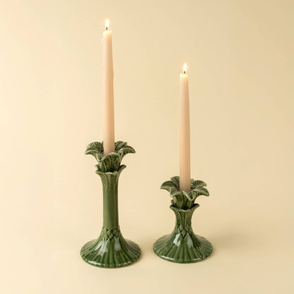 Two green ceramic candle holders with lit candles on a beige background