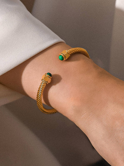 Gold bracelet with green gemstones on a wrist against a neutral background