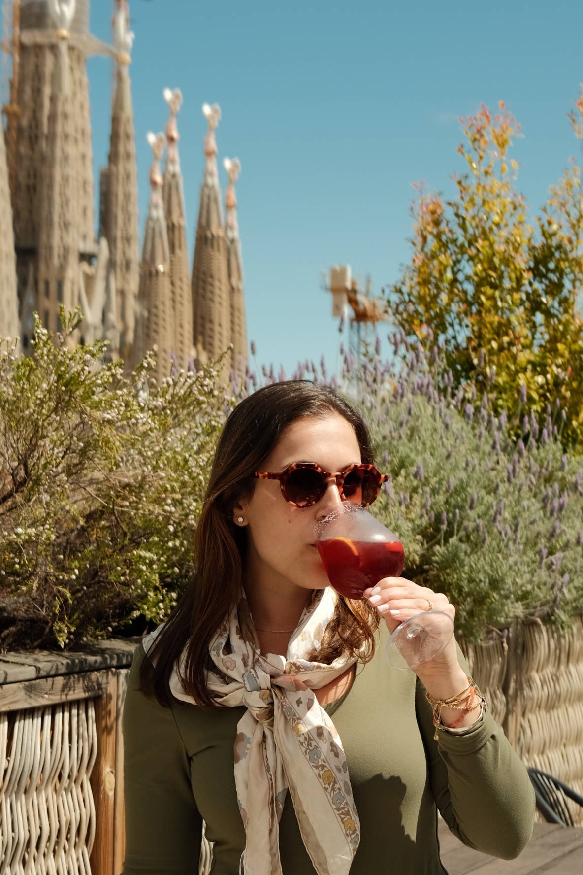 Woman drinking red wine with a scenic background of a cathedral and trees.