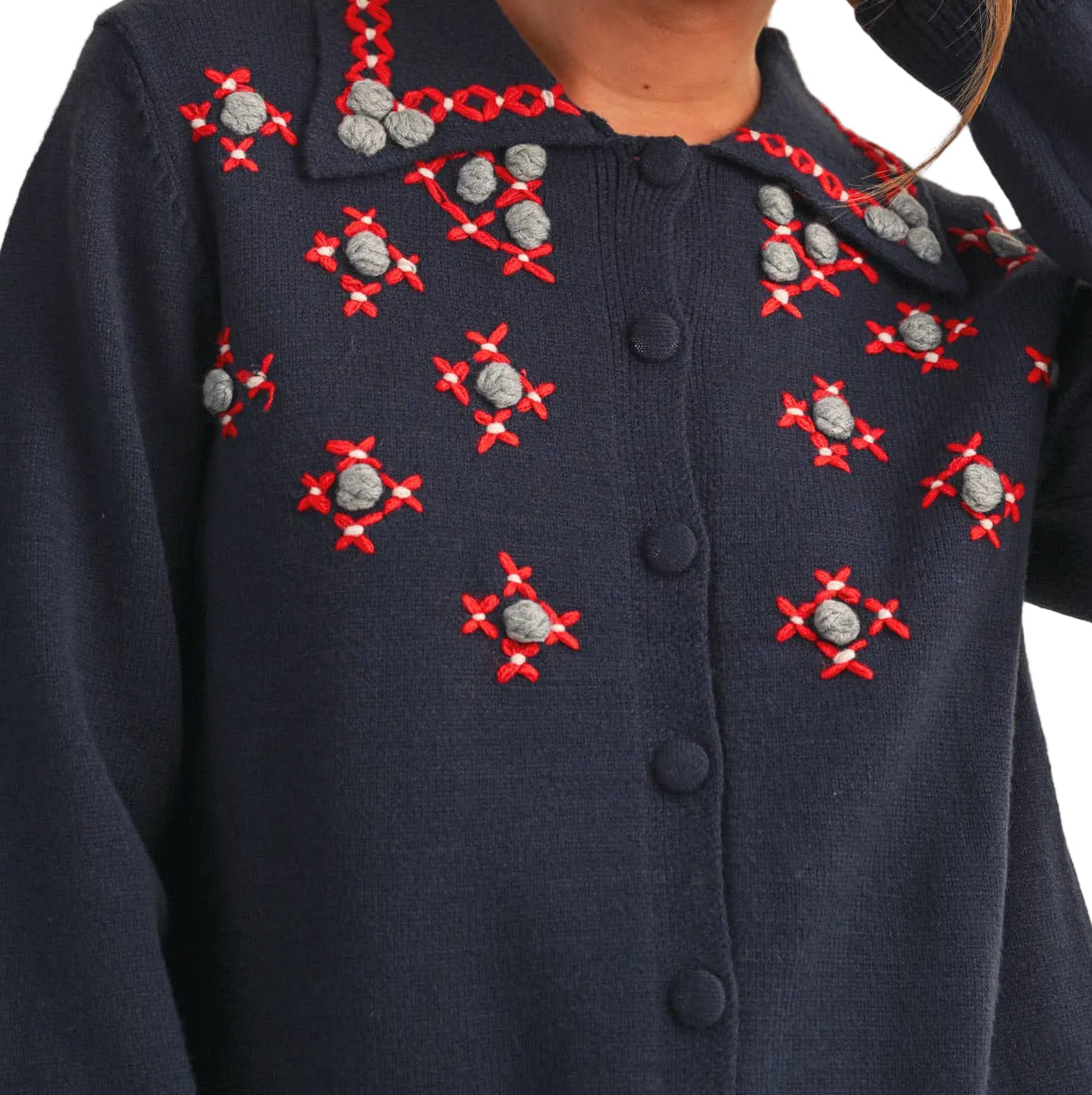 A woman wearing a navy blue knit cardigan sweater with red and silver embroidered starburst patterns and a red-and-silver embroidered collar, photographed against a plain beige background.