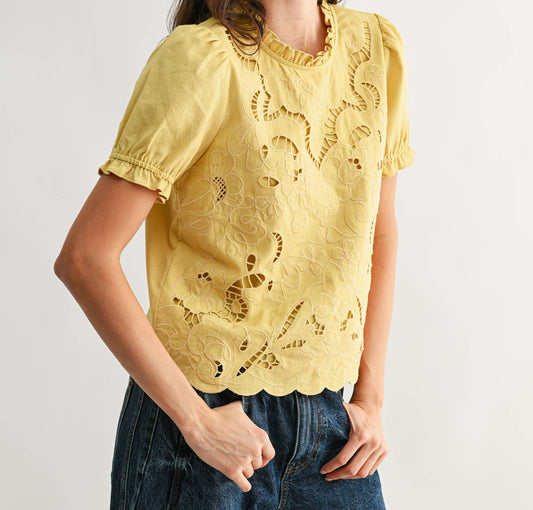 Woman wearing a yellow lace top and blue jeans against a plain background