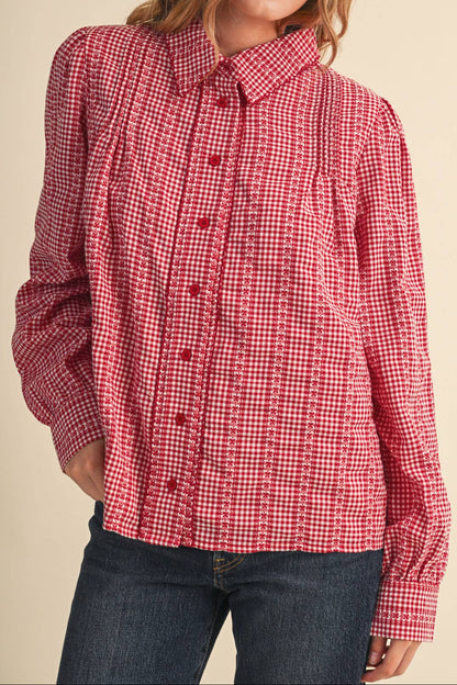 A woman wearing a red and white gingham long-sleeve button-up shirt with dark blue jeans, photographed against a solid beige background.