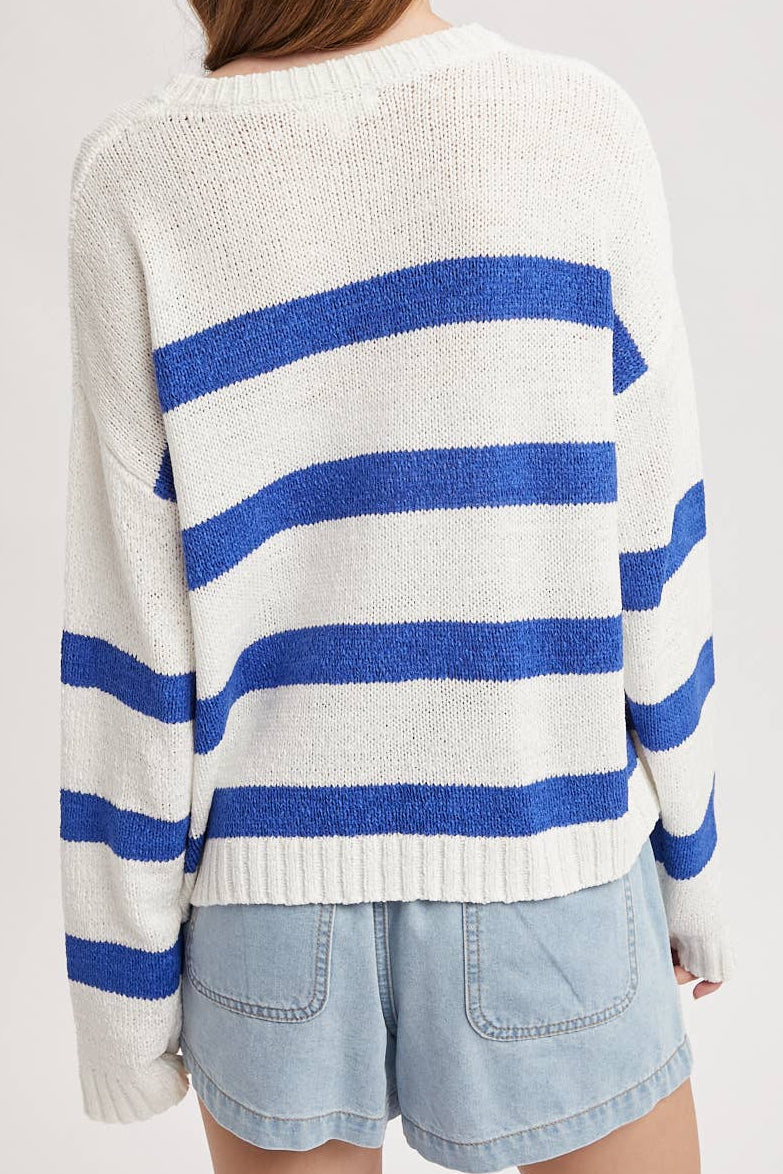 Person wearing a white sweater with blue stripes and denim shorts on a plain background