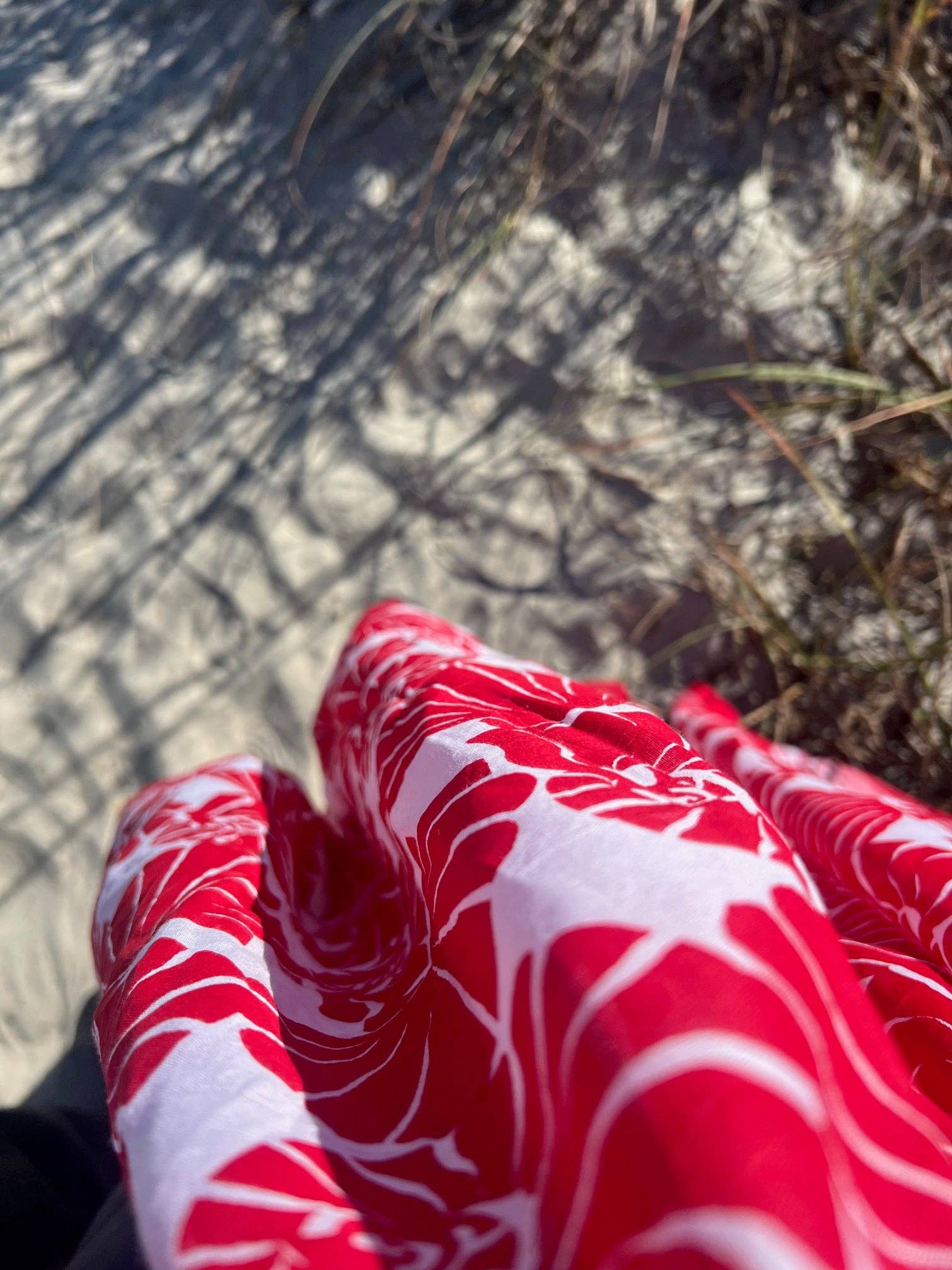 Red and white patterned fabric held over a sandy and grassy ground.