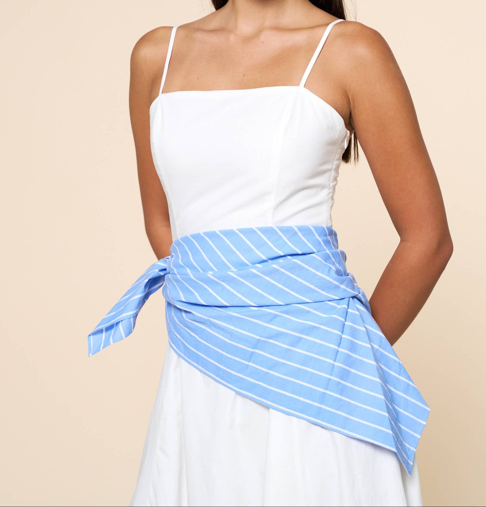 Woman wearing a white top and blue striped skirt against a beige background