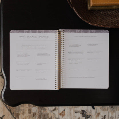 Open spiral-bound book on a dark surface with text and questions visible