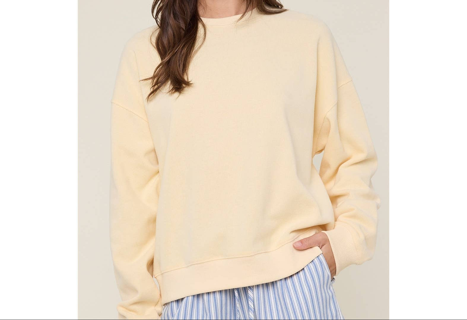 Woman wearing a light yellow sweatshirt and a patterned bucket hat on a beige background
