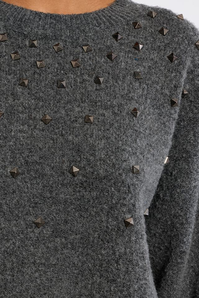 Close-up of a dark gray knit sweater with pyramid stud embellishments on the chest and shoulders.