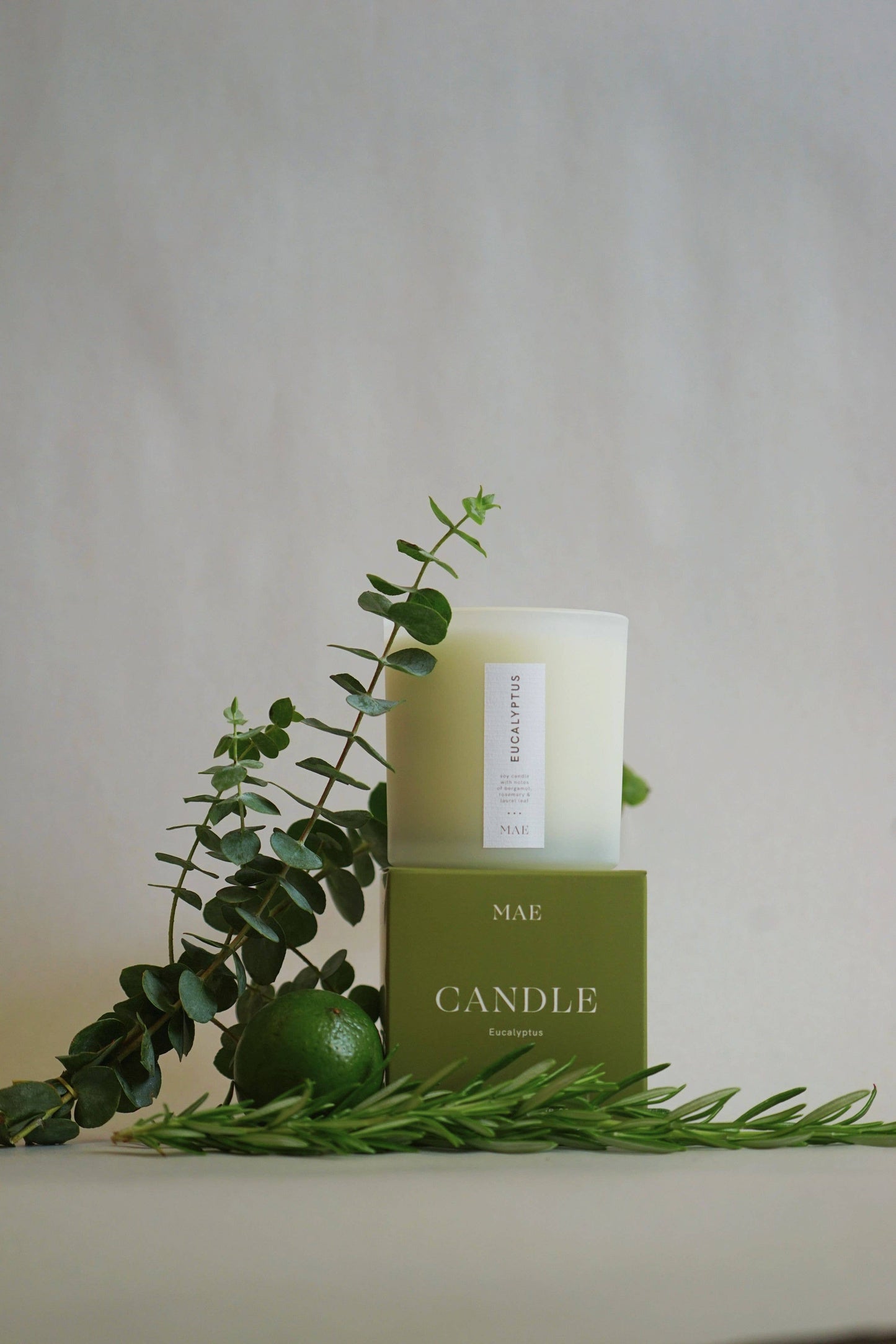 Green candle with eucalyptus leaves on a neutral background