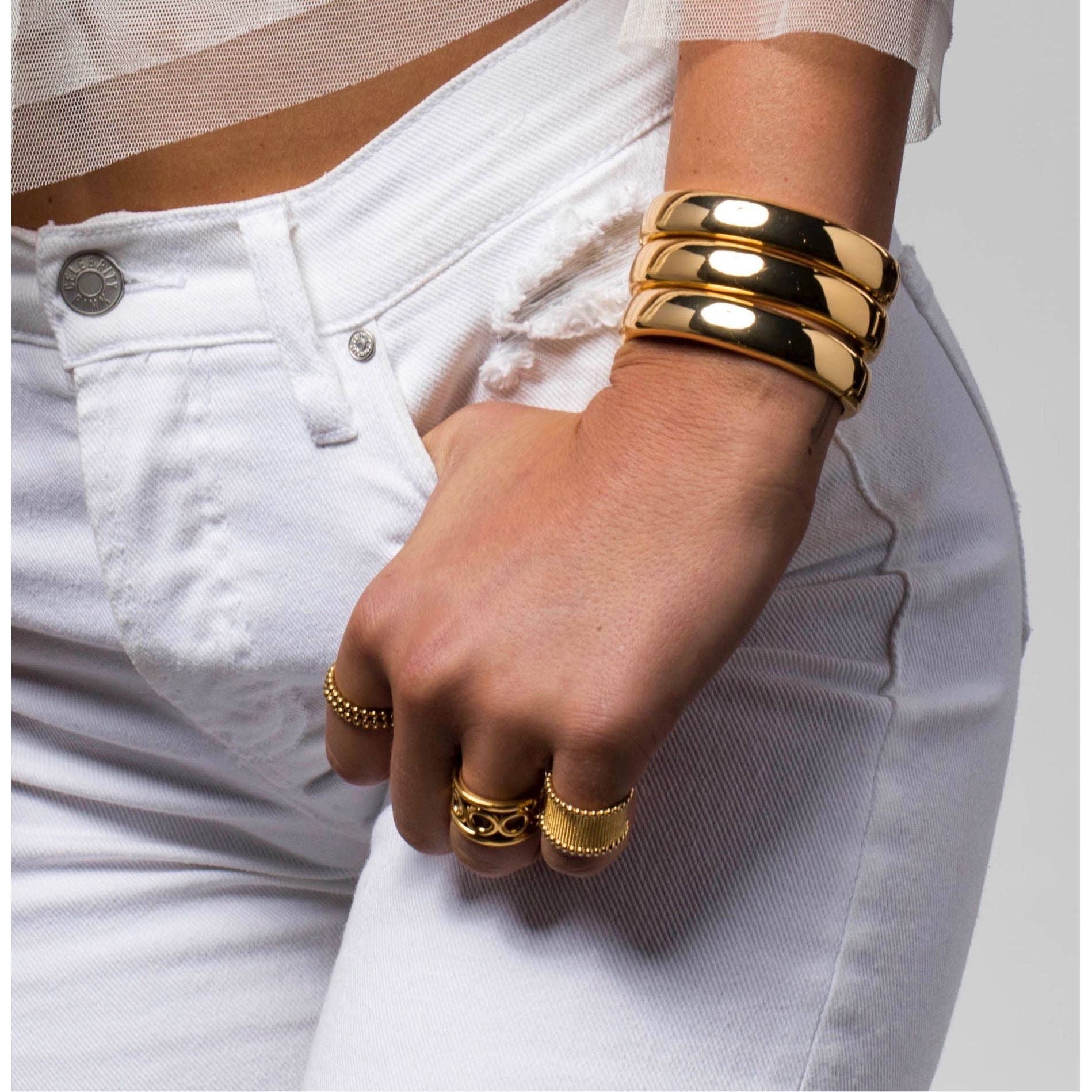 Gold bracelets and rings on a hand with white jeans