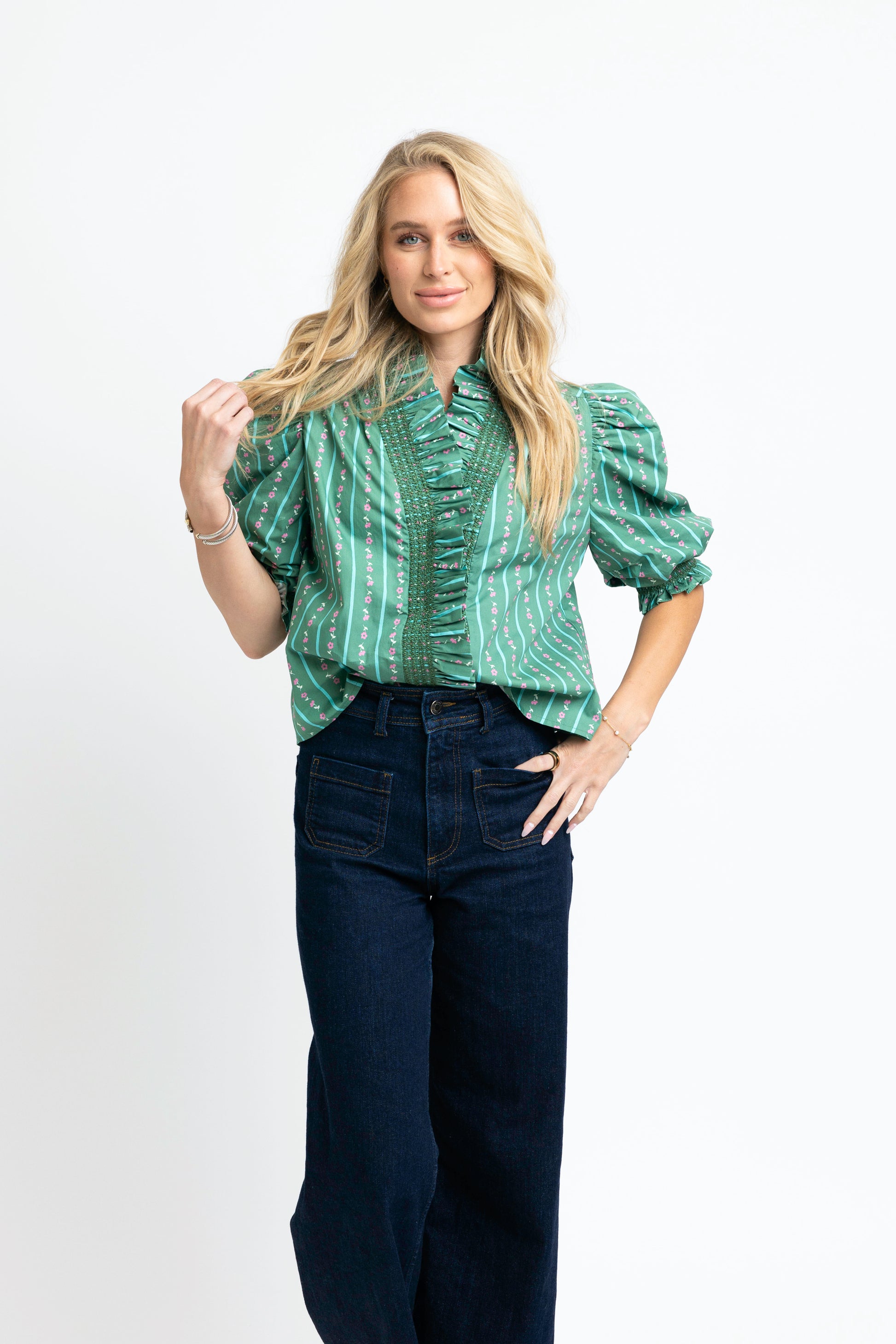 Woman wearing a green patterned blouse and dark jeans on a white background