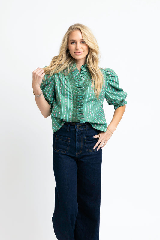 Woman wearing a green patterned blouse and dark jeans on a white background