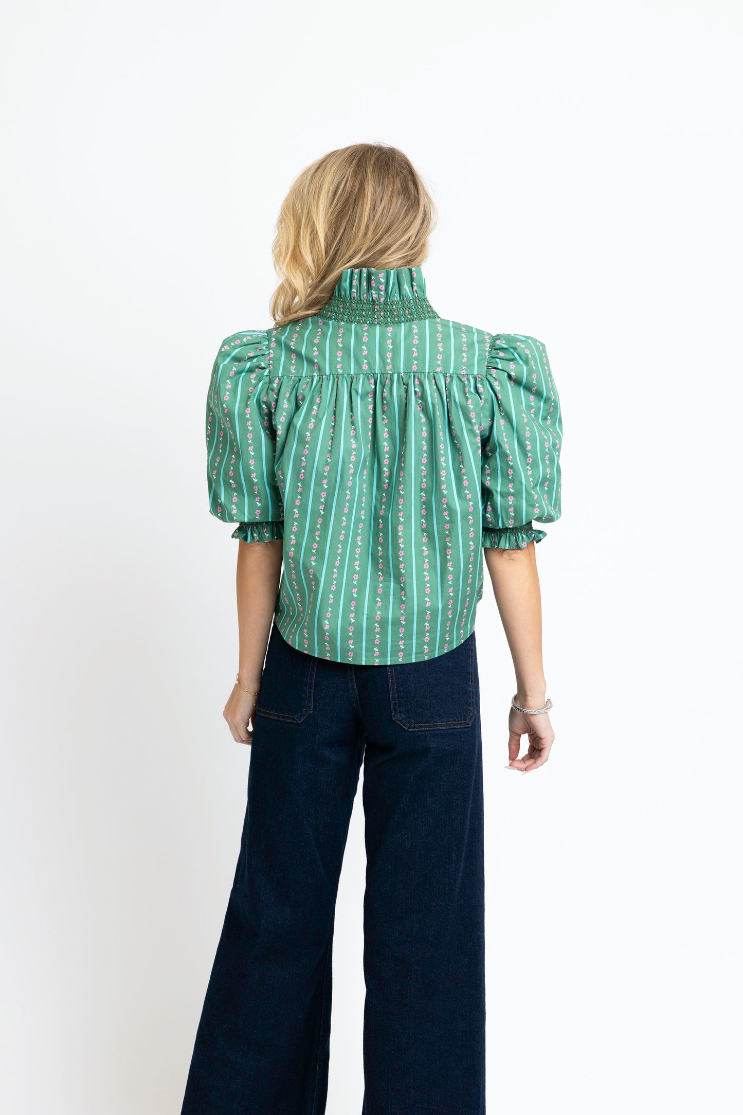 Person wearing a green patterned blouse and dark blue jeans on a white background