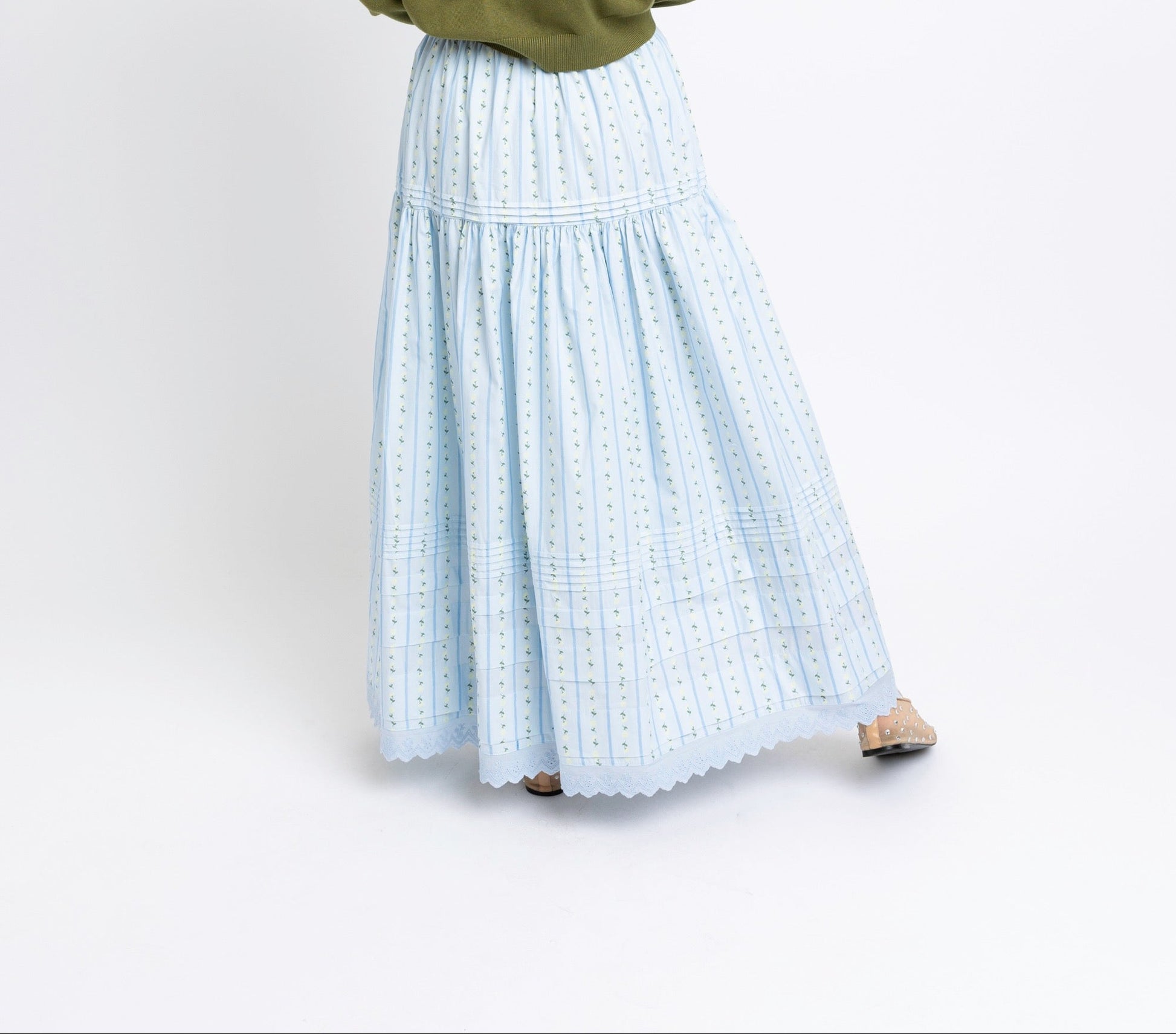 Person wearing a green sweater and light blue plaid skirt on a white background