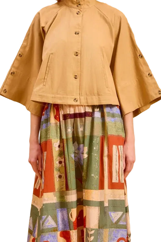 Woman wearing a beige jacket and colorful patterned skirt against a beige background