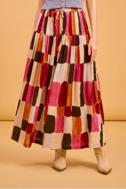 Woman wearing a colorful checkered pants and patterned top against a beige background
