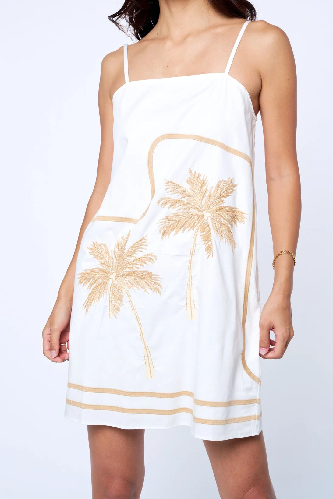 Woman wearing a white dress with palm tree designs on a plain background