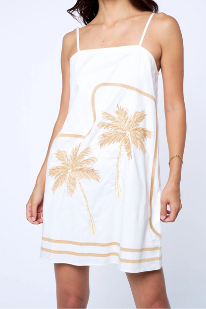 Woman wearing a white dress with palm tree designs on a plain background
