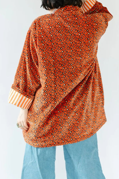 A person shown from the back wearing an oversized orange patterned cardigan over a striped shirt, light blue wide-leg jeans, against a plain light gray studio background.