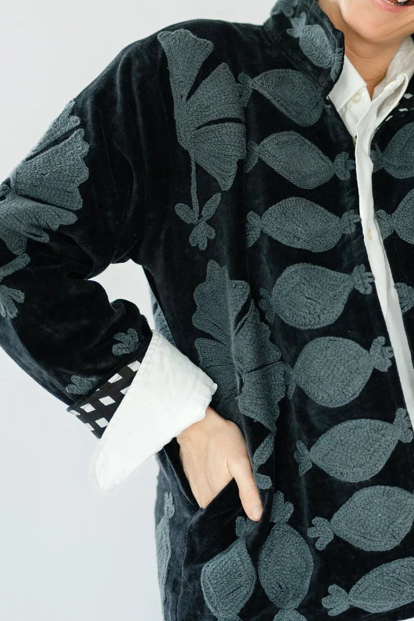 A woman wearing a black and gray patterned fleece jacket with white cuffs and a white shirt underneath, posing against a light gray background.