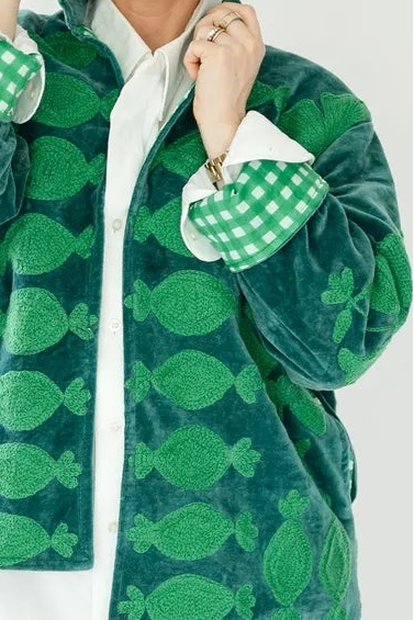 A woman modeling a green patterned zip-up jacket with green-and-white checkered cuffs, , against a plain white studio background.