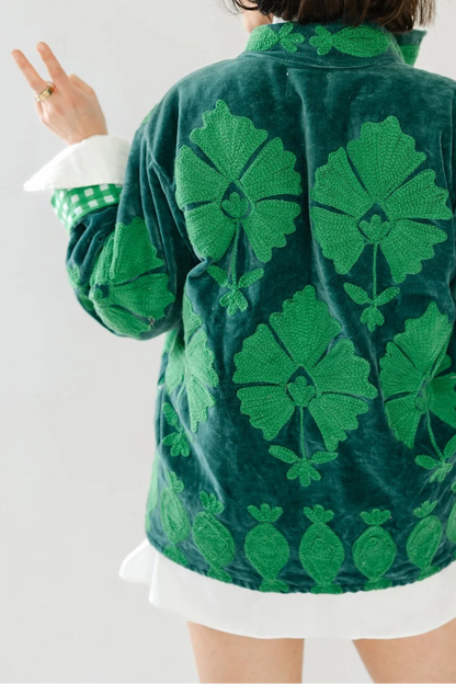 A person shown from behind wearing a green velvet jacket with a large green floral pattern, posed against a plain white background.
