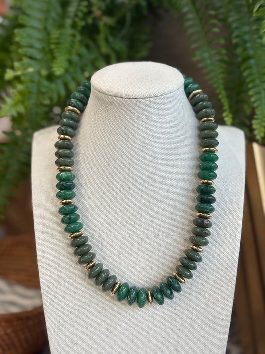 Green beaded necklace on a mannequin bust with a fern background
