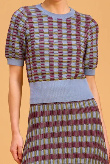 A woman modeling a matching set with a blue, green, and burgundy checkered pattern, featuring a solid light blue waistband and short blue sleeves, set against a solid beige studio background.