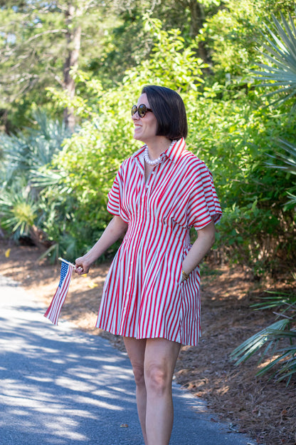 Woman in a red and white striped dress walking outdoors with greenery in the background