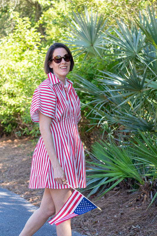 Woman in a red and white striped dress holding an American flag outdoors.