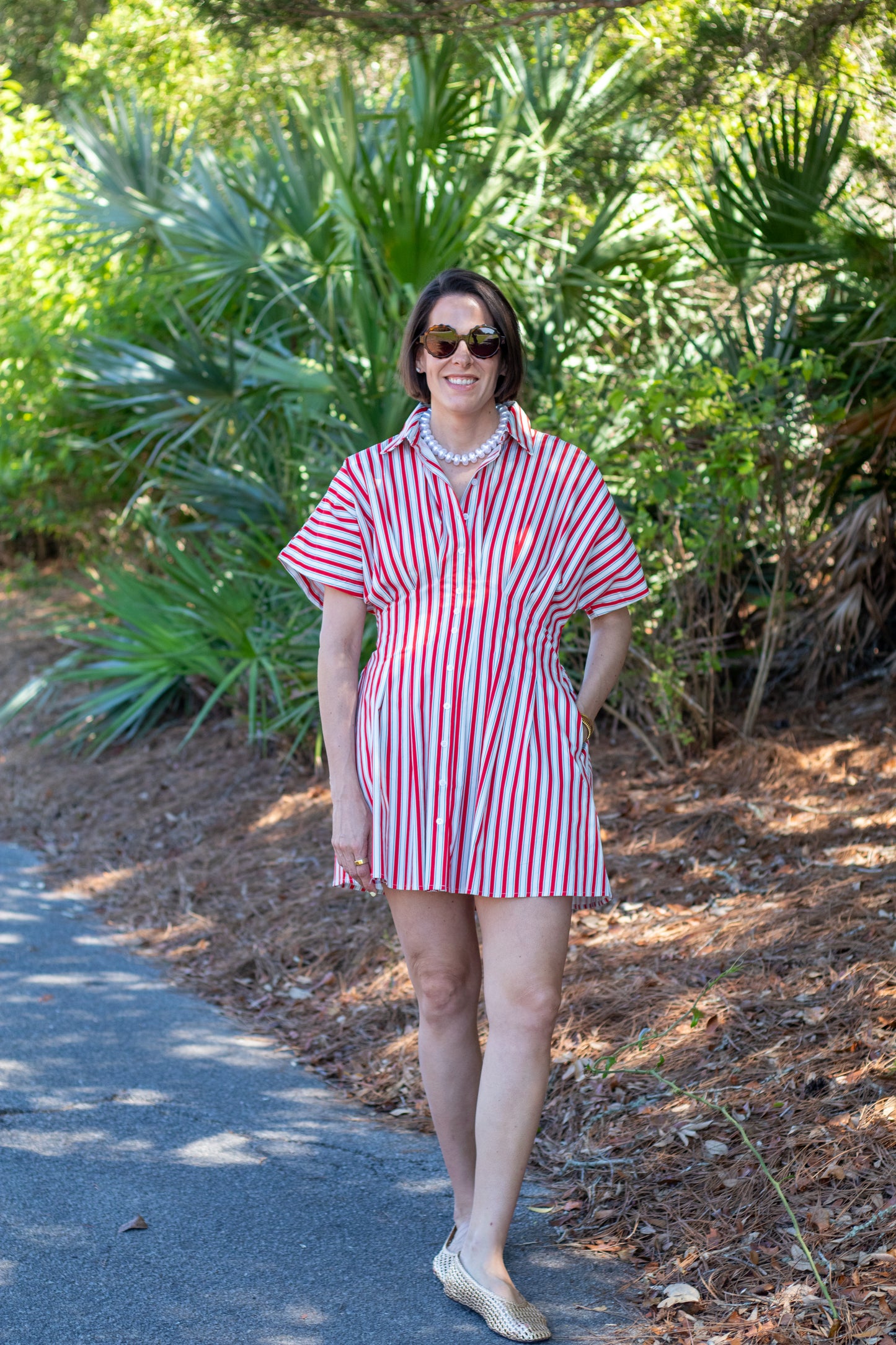Woman in a red and white striped dress standing on a path with greenery in the background